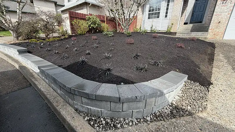 Concrete block retaining wall with new plantings and brown hemlock mulch at a Rock Creek Portland Oregon home